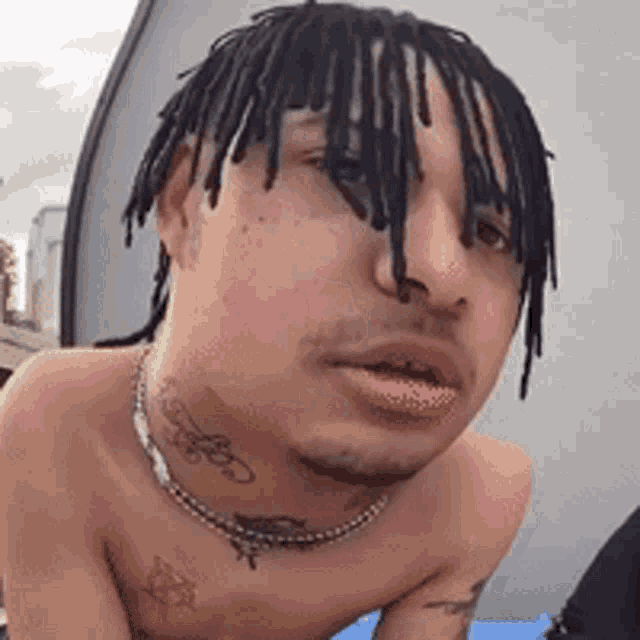 a shirtless man with dreadlocks is wearing a necklace around his neck .