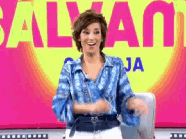 a woman in a blue shirt is dancing in front of a sign that says salvam