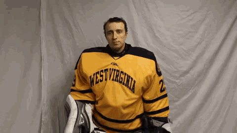 a man wearing a yellow west virginia jersey is standing in front of a white curtain .