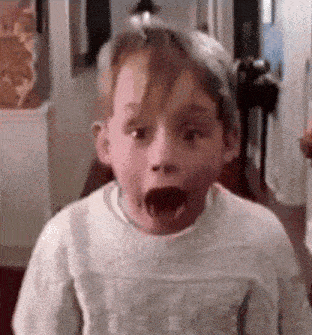 a young boy in a white sweater is making a surprised face .