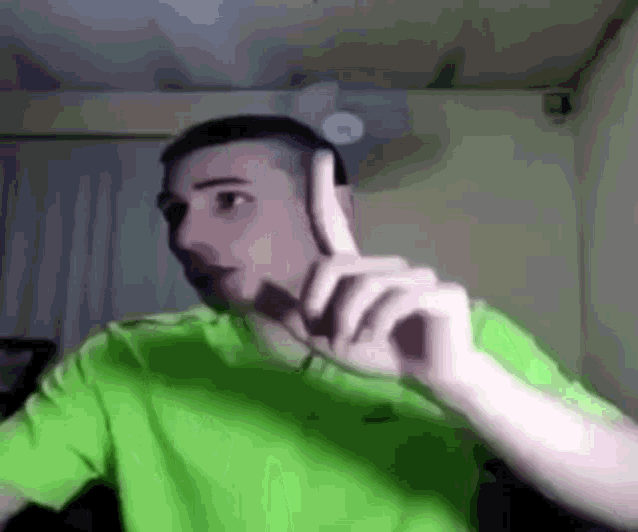 a man in a green shirt is making a funny face while holding his finger up .