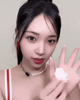 a woman wearing a pearl necklace and a red and white striped tank top is holding something in her hand