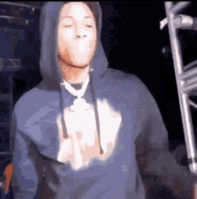 a man in a blue hoodie is standing on a stage with his eyes closed and his mouth open .