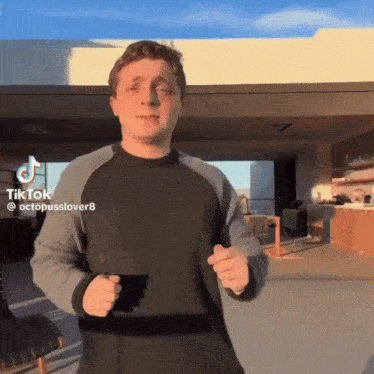 a man in a black and grey sweater is dancing in front of a building with a tiktok watermark on the bottom