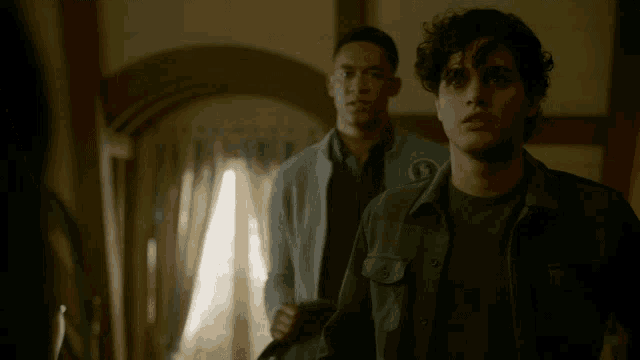 two men are standing in a room and one has a patch on his jacket that says s