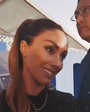 a woman with a ponytail and a man with glasses looking at her