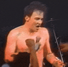 a shirtless man is singing into a microphone while playing drums .