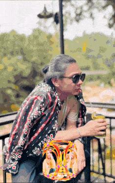 a man wearing sunglasses sits at a table with a picture of two women behind him