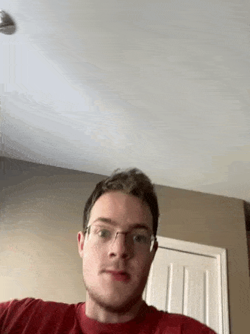 a man wearing glasses and a red shirt is standing in front of a door in a room .