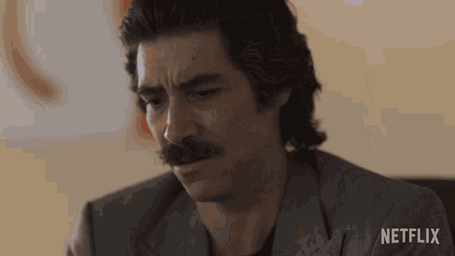 a man with a mustache is sitting in front of a wall that says netflix