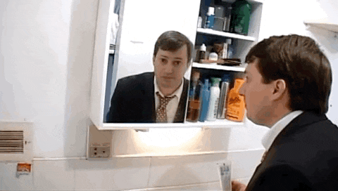 a man in a suit and tie looks at his reflection in a mirror