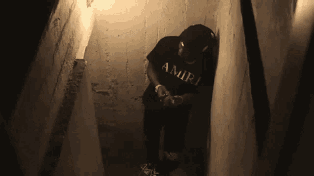a man wearing a black shirt that says amiri is standing in a dark room