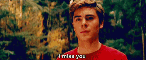 a young man in a red shirt is standing in front of a forest and saying `` i miss you '' .