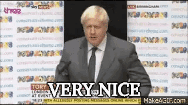 a man in a suit and tie is standing in front of a microphone and says very nice
