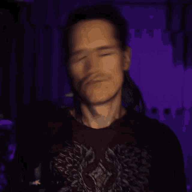 a man with a ponytail is wearing a purple shirt