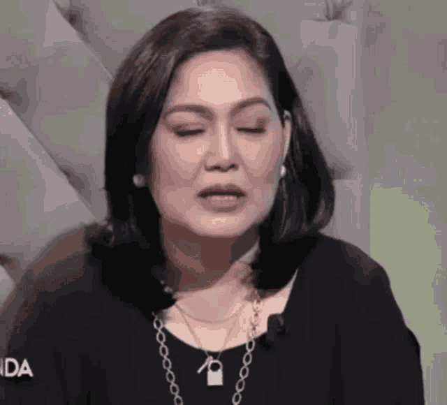 a woman with her eyes closed wearing a black shirt and a necklace .
