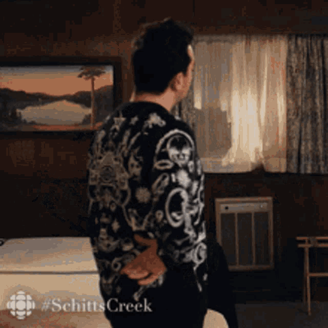 a man in a sweater from schitts creek is standing in a bedroom