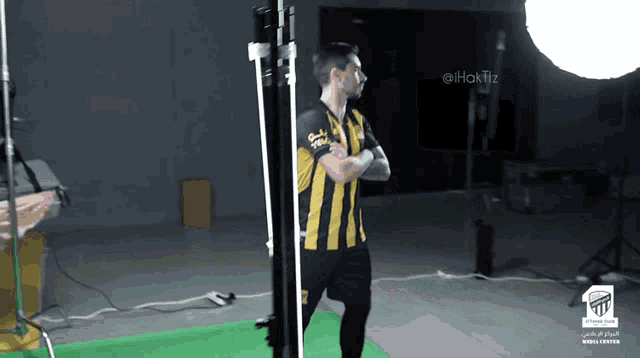 a man in a yellow and black striped shirt stands with his arms crossed in front of a green screen