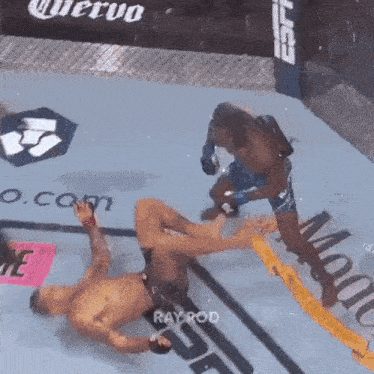 a man is laying on the ground in a boxing ring while another man kicks him in the face .