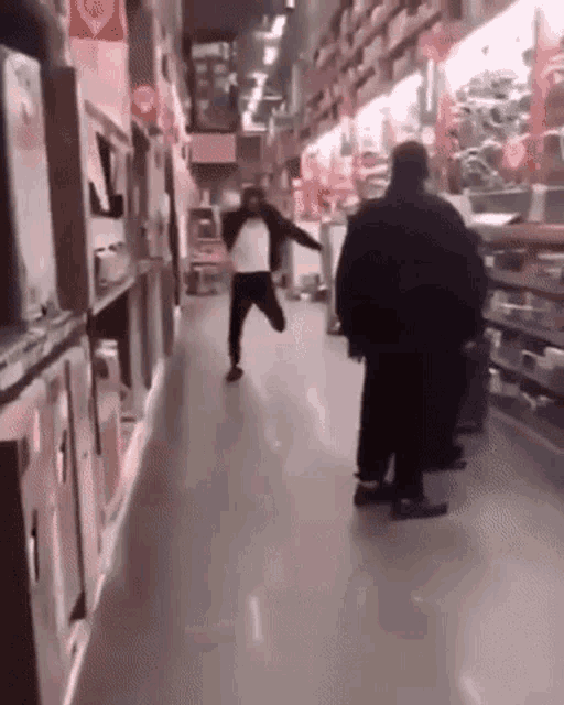 a man is running down a hallway in a store while a man stands behind him .