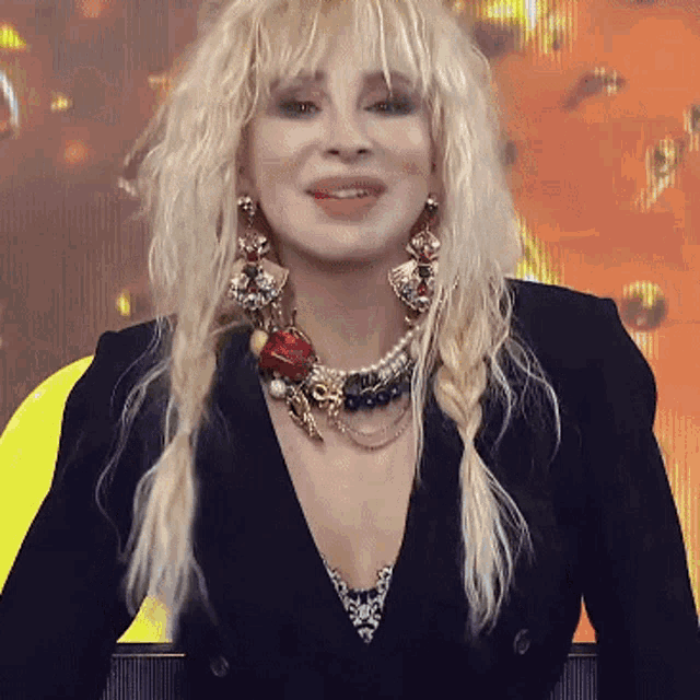 a woman with blonde hair wearing a black jacket and a pearl necklace