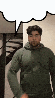 a man in a green hoodie is standing in front of a staircase with a speech bubble above him