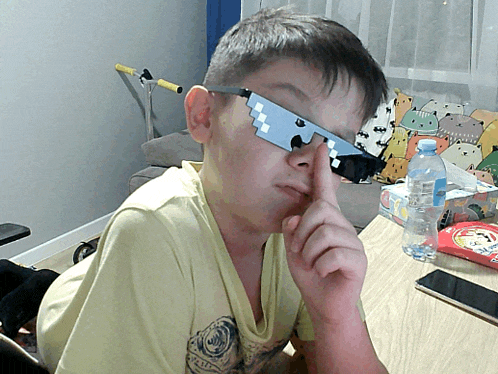 a boy wearing sunglasses that look like a gun is sitting at a desk