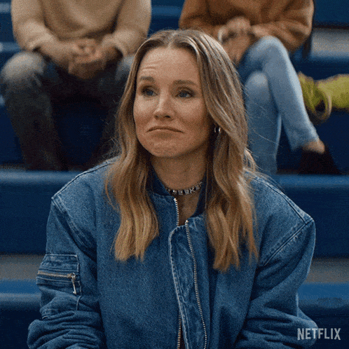 a woman in a denim jacket is sitting in a bleacher with a netflix logo behind her