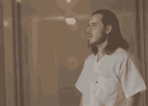 a man with long hair is wearing a white scrub top with a black pocket