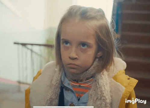 a little girl wearing a yellow jacket and a scarf is looking up at the camera with imgplay written below her