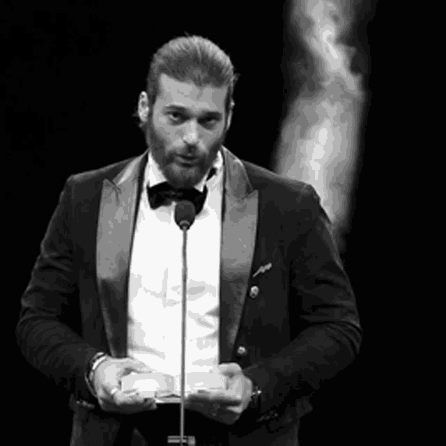 a black and white photo of a man in a tuxedo holding a microphone