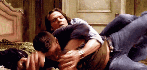 two men are laying on top of each other on a bed and hugging each other .
