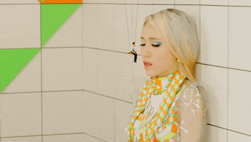 a woman in a colorful dress is leaning against a white tile wall