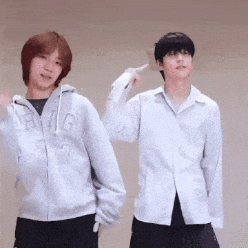 two young men are standing next to each other in a room and pointing at each other .