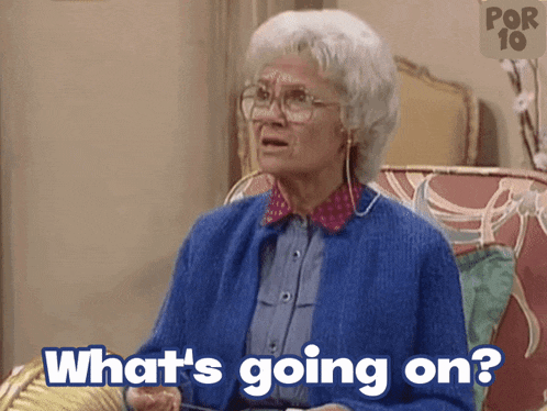an elderly woman in a blue sweater is sitting in a chair and says what 's going on
