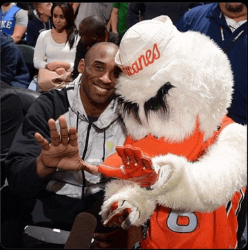 a man sitting next to a mascot wearing a hat that says miami on it