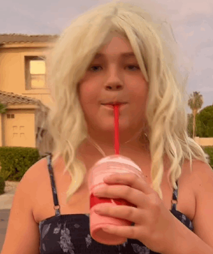 a young girl in a blonde wig is drinking a milkshake through a straw .