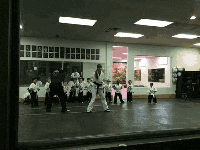 a group of kids are practicing martial arts in a gym with a sign on the wall that says ' karate '