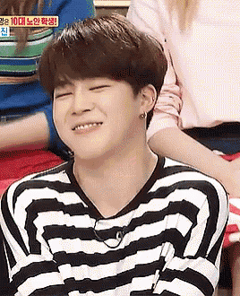 a young man in a black and white striped shirt is smiling while sitting in front of a group of people .