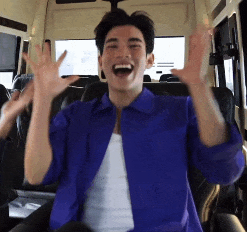 a man in a blue shirt is sitting in a bus with his arms in the air .