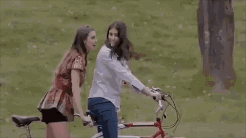 a group of people are riding bicycles in a park . one of the girls is kissing another girl on the cheek .