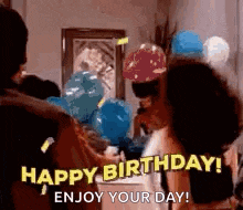 a group of people are standing around a table with balloons and saying `` happy birthday ! enjoy your day ! ``