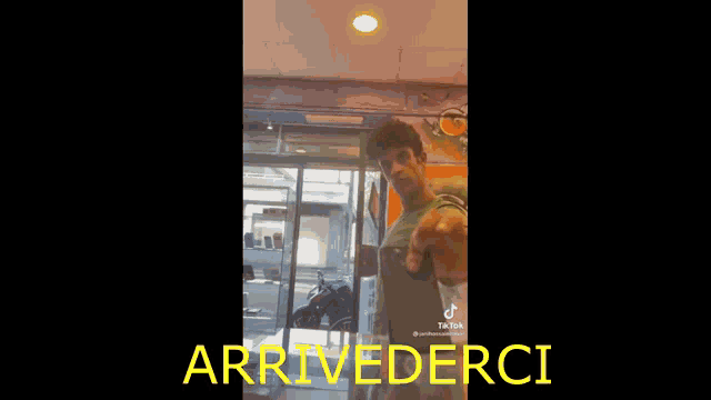 a man is standing in front of a store with the words arrivederci on the bottom of the screen .
