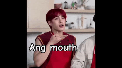 a young man with red hair is making a funny face in a kitchen while wearing a red shirt .