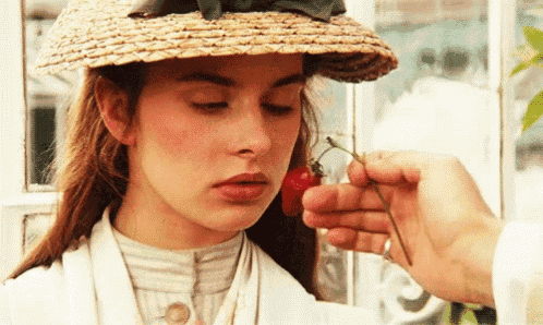 a woman wearing a straw hat is being smelled by a man holding a flower .