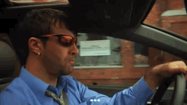 a man wearing sunglasses and a blue shirt driving a car