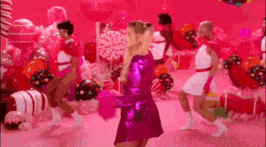 a woman in a pink dress is dancing in a room filled with pink balloons and candy .