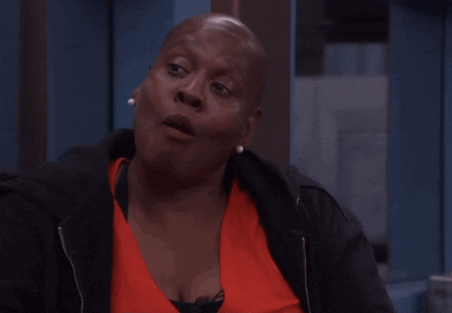 a woman wearing an orange shirt and a black jacket is making a funny face