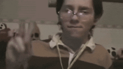 a man wearing glasses and headphones is making a peace sign with his hand .