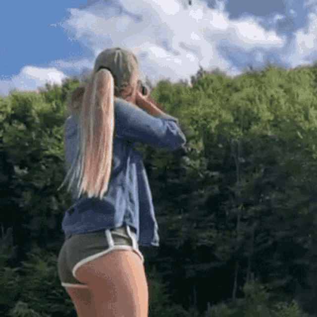 a woman is standing in front of a forest wearing shorts and a hat .